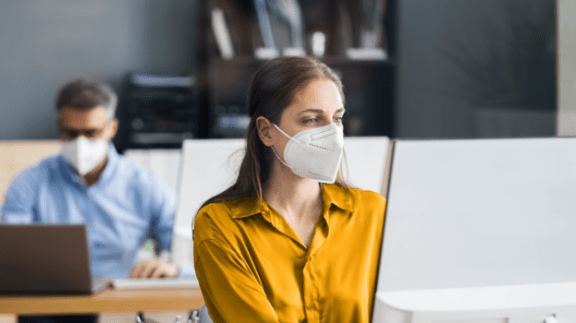 professional woman in yellow shirt wear mask at a computer