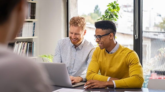 two men sitting in front of a computer simling