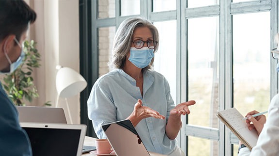 woman in mask talking person with clipboard and man with computer