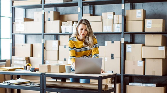 women wearing yellow leaning over computer surrounded by boxes