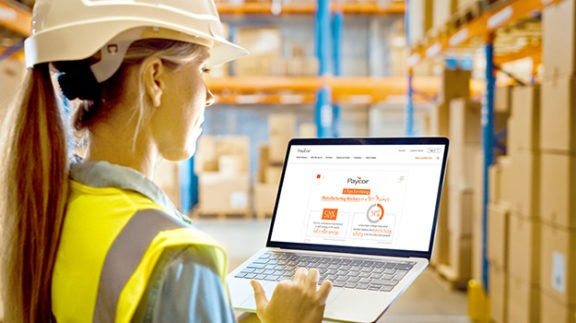 manufacturing woman using a laptop in a hardhat and construction vest surrounded by boxes