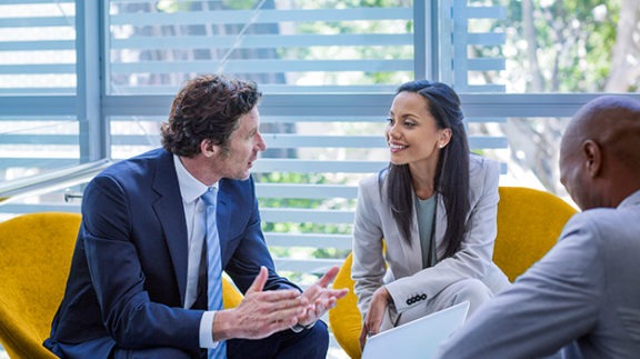 three professionals sitting in yellow chairs discussing business