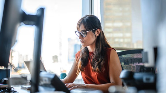 woman in glasses sitting at a desk at a laptop