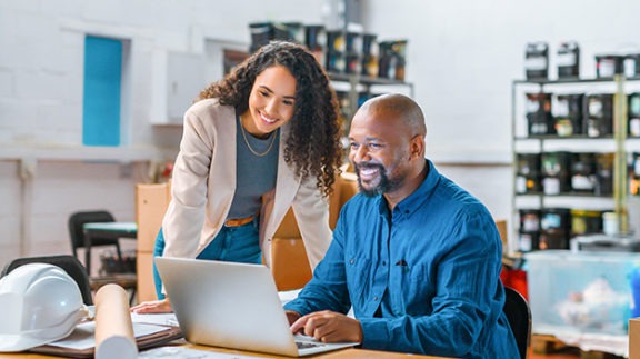 two smiling workers looking at laptop screen in office